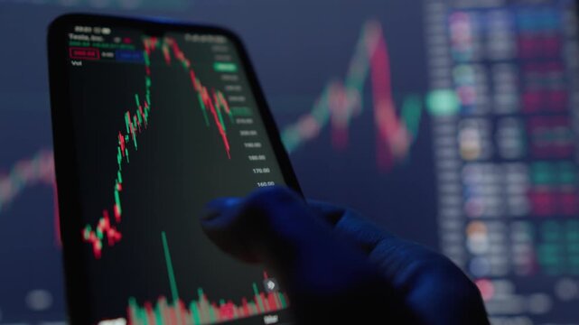 A dedicated trader intently focuses on a mobile phone that shows various stock charts, intricately revealing fluctuations in market trends illuminated by vibrant and colorful digital displays