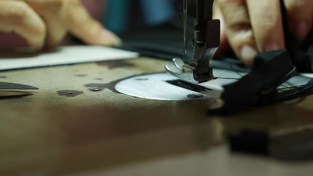 A sewing machine stitches fabric in close view near visible metal machine parts. Artisan work.