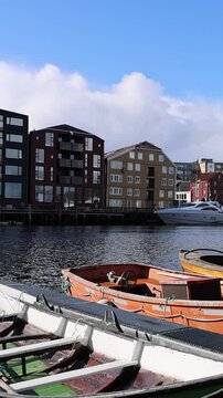 View of traditional colorful wooden warehouses along the Nidelva river with small boats moored in the foreground under a blue sky in Trondheim, Trondelag, Norway.