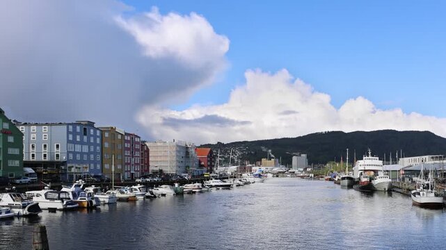 View of colorful wooden warehouses along the Nidelva river with boats moored in the harbor under a cloudy sky in Trondheim, Trondelag, Norway.