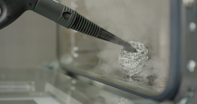 Worker sanitizing commercial kitchen oven interior using a high pressure steam nozzle brush tool