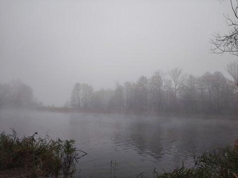 Heavy morning fog evaporating over a calm river surface in late autumn
