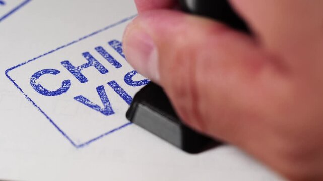 Macro video frame of a stamp pressing "REJECTED" onto a China visa application document.