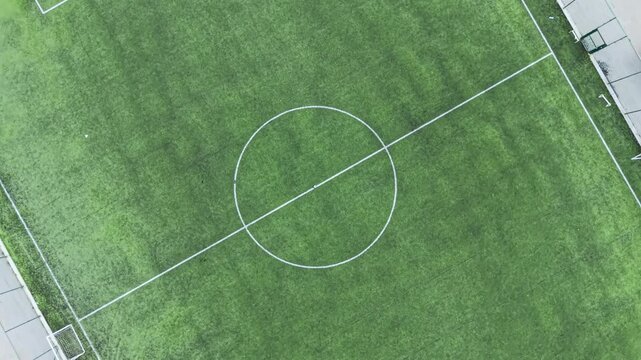 The view from above shows a soccer field with bright green turf and white lines. The center circle is visible. The scene is empty and well kept, likely used for sports activities.
