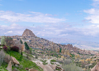 Obraz premium A scenic view of the historic Uchisar Castle and unique fairy chimney rock formations in the Cappadocia region of Turkey under a blue sky.