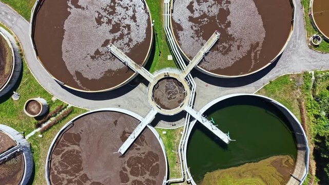 Workers manage the water treatment process in large circular tanks at a facility. Different stages of water flow are seen during the daytime.