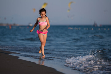Fototapeta premium Happy girl running along beach shoreline with ocean waves
