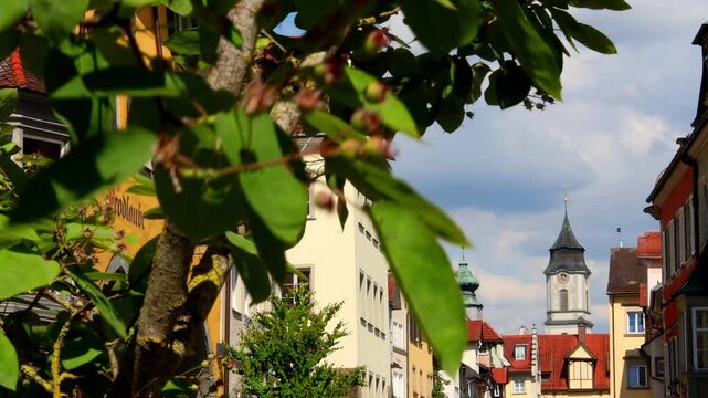 View of the historic town of Lindau with the tower of St. Stephan's Church rising above colorful buildings and lush green foliage in Lindau, Bavaria, Germany.