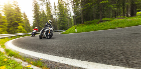 Obraz premium Sport motorcycle rider cornering on a winding mountain pass. Motion blur and dynamic perspective emphasize speed, control, performance riding and scenic road adventure.