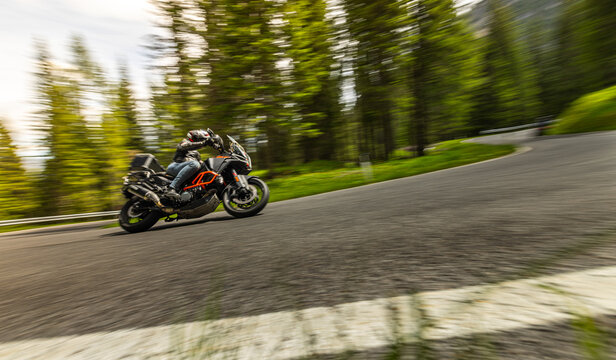 Touring motorcycle rider navigating a winding mountain road through forest scenery. Motion blur and dynamic perspective emphasize travel, adventure and freedom on two wheels.