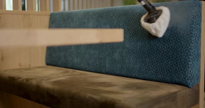 Worker sanitizing blue fabric backrest of restaurant booth seating with professional steam tool nozzle