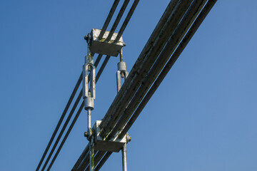 Fototapeta premium Close-up of steel cable tensioner and turnbuckle on a suspension bridge against clear blue sky. Structural engineering detail of bridge cable system. Industrial infrastructure and architecture concept