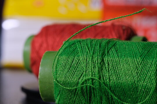 Close-up of red and green sewing thread spools with selective focus, perfect for tailoring, craft, and textile concepts