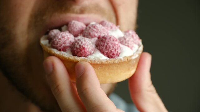 Extreme close up bearded man mouth eating delicious tartlet with fresh raspberries and cream, savoring every bite of sweet dessert enjoying delightful treat. Bearded man eating raspberry cream tartlet