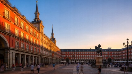 Obraz premium Plaza Mayor at Dusk: A grand European plaza, bathed in the warm light of sunset, showcases stunning historical architecture with ornate balconies and towers, creating a vibrant atmosphere.