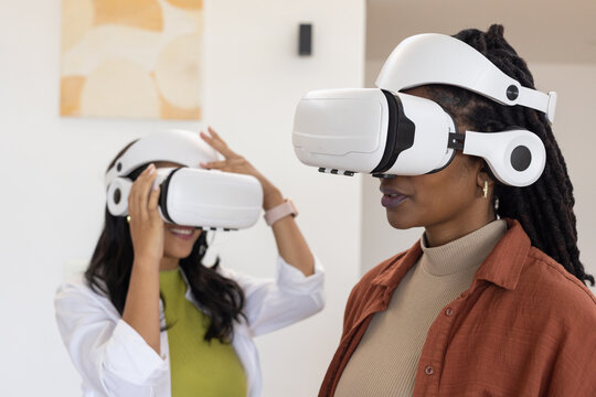 African women testing white VR headsets wearing rust jacket and adjusting smartwatch in bright room