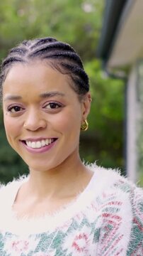 Vertical video: Smiling woman reacting to camera, blinking, tilting in yard, fuzzy knit, gold hoops