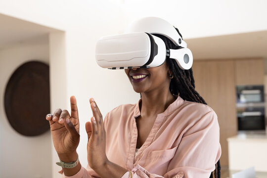 Adult woman wearing white VR headset and blouse, manipulating virtual controls in open-plan kitchen