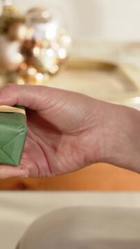 Vertical video: Holding right hand rotating and releasing green gift on wooden table with ornaments