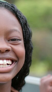 Vertical video: Smiling girl shifting to laugh at park railing with green tie, hand showing at side