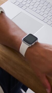 Vertical video: Camera shifting, left wrist turning on desk by laptop, preparing to type with watch