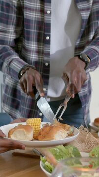 Vertical video: Carving man in plaid slicing poultry to serve plate held at home with knife, fork