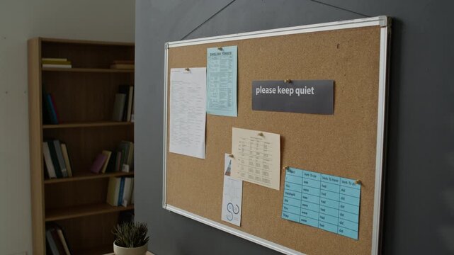 Corkboard hanging on wall displaying English grammar sheets and please keep quiet sign in empty classroom. Footage is ideal for language school promotions and ESL learning campaigns