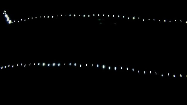 Rows of small white decorative string lights glowing against a dark black background