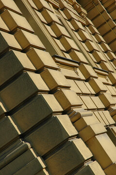 Side angle diagonal view of a historical neoclassical building facade showing textured rustic plaster blocks with geometric shadow lines.