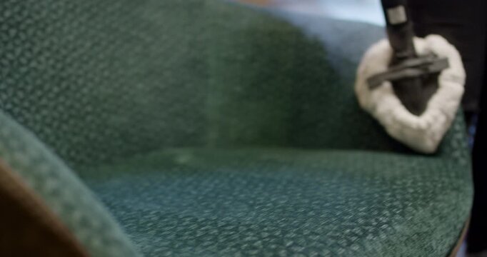 Close up view of steam tool extension cleaning cushion surface of a green fabric armchair