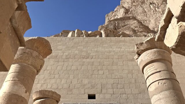 A low-angle, symmetrical perspective showing the monumental stone architecture at the Mortuary Temple of Hatshepsut (Deir el-Bahari) in Luxor, Egypt.