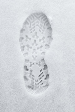 A single bootprint in fresh snow reveals a clear tread pattern and solitary winter step, evoking cold, quiet outdoors, hiking and travel, with texture, contrast and the trace of human movement
