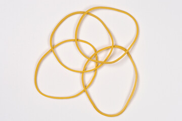 Fototapeta premium A top down shot shows several thin yellow rubber bands overlapping and tangled together on a plain white background.