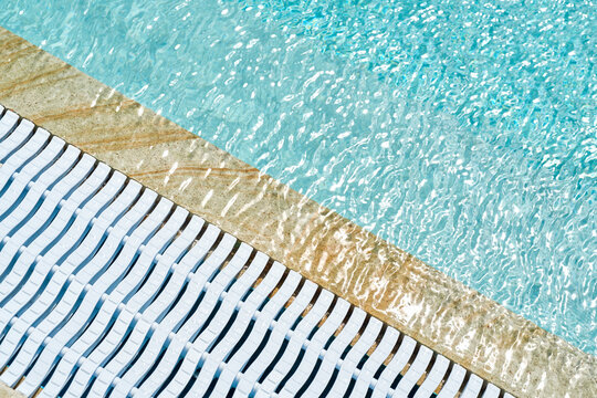 The edge of a pool with blue water and a white plastic drain grate.