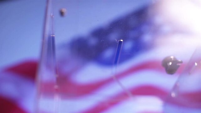 Hand putting a ballot paper into a transparent ballot box on the background of the USA flag