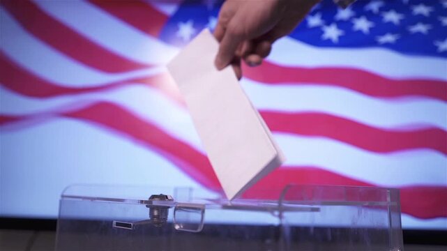 Hand putting a ballot paper into a transparent ballot box on the background of the USA flag