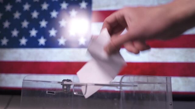 Hand putting a ballot paper into a transparent ballot box on the background of the USA flag