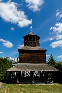 Traditional wooden church bell tower in Chortkiv, Ternopil region, Ukraine, standing beneath a bright blue sky with scattered clouds.