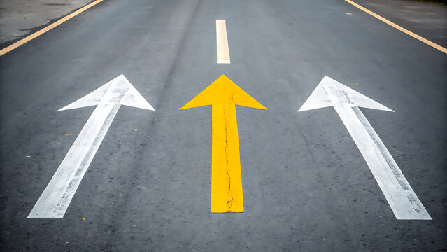 Asphalt road surface with a bright yellow arrow painted in the center and two white arrows on both sides pointing forward in the same direction