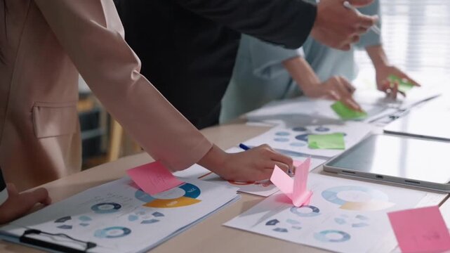 Group of diverse business colleagues collaborating during financial strategy meeting using charts and sticky notes