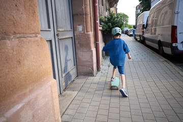 Young boy in blue outfit rides a skateboard on a paved sidewalk wearing a helmet © 4Max