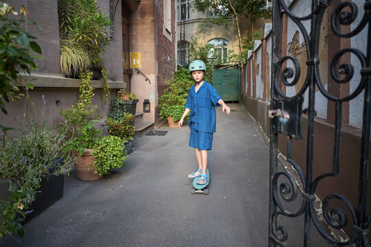 Young child in protective helmet rides a skateboard down a narrow urban alleyway