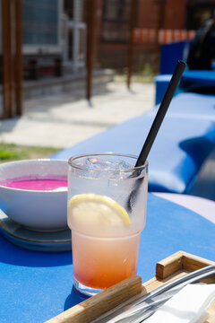 Cold refreshing grapefruit lemonade with ice and a lemon slice on a blue table at an outdoor cafe terrace
