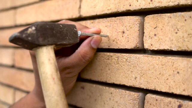 Person using metal hammer to drive nail into brick wall a close up view of a person's hand holding small against wall, ready