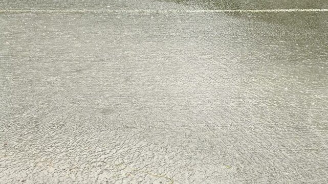 heavy rain beats down onto a completely flooded asphalt street. The constant downpour creates ripples across the sweeping sheet of water, resulting in a loud pattering and splashing sound.