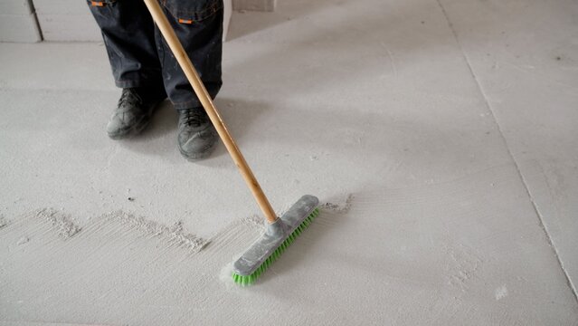 Worker sweeping concrete floor with green bristle broom in construction site