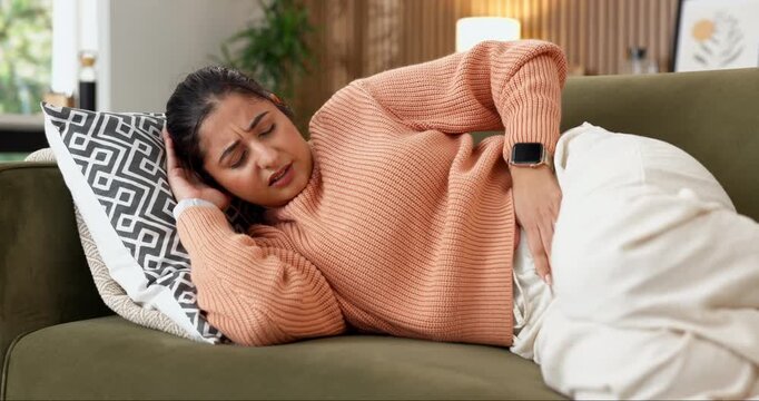 Sick, pain and woman with stomach ache on sofa for menstruation, discomfort or agony in home. Endometriosis crisis, person or belly inflammation in house from ovulation cycle, IBS or abdominal cramps