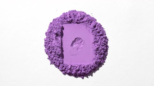Top perspective capture of a heap of violet powder with a rectangular shape pressed into a faint grey backdrop, lit with orbiting directional light casting dynamic shadows