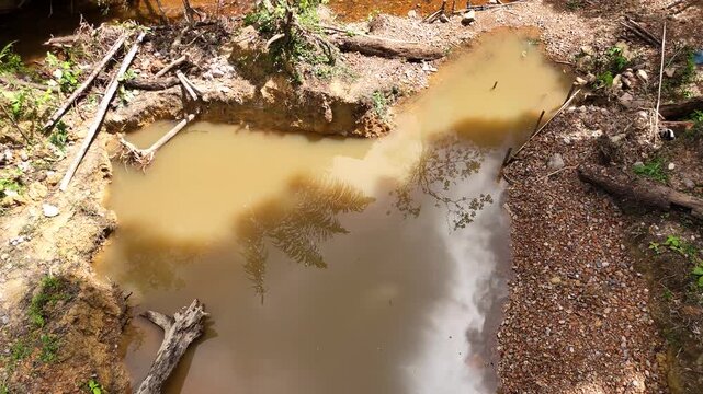 Aerial footage of a muddy water pond and excavation traces at an abandoned gold mining garimpo area near Cacao, French Guiana.