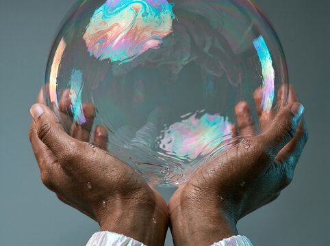 Hands Holding Iridescent Bubble Against Gray Background